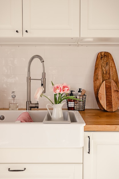 Premium Photo White Ceramic Sink With Faucet Hose And Pink Ranunculus Flowers In It In A Modern Scandinavian Style Apartment Cozy Home Decoration Concept Wooden Counter With Various Kitchenware