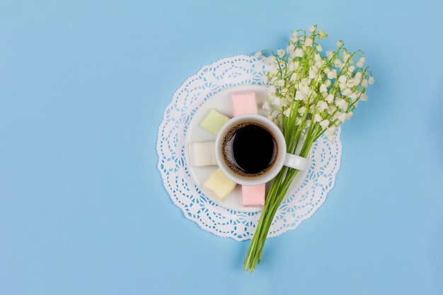 ソーサー マシュマロ 青の背景にユリの谷の花の花束にコーヒーカフェラテの白いカップ プレミアム写真