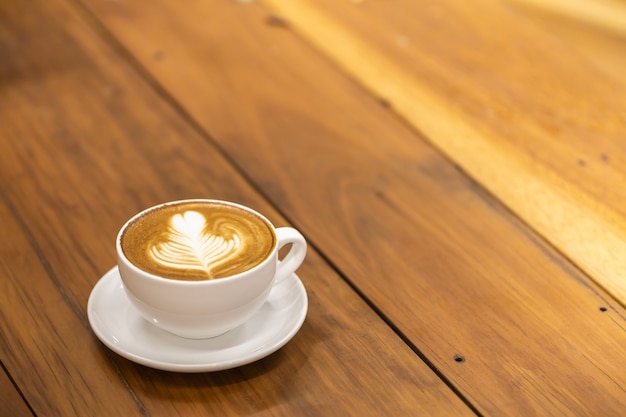 木製のテーブルにハートとフラワーアートのホットコーヒーカフェラテの白いカップ プレミアム写真