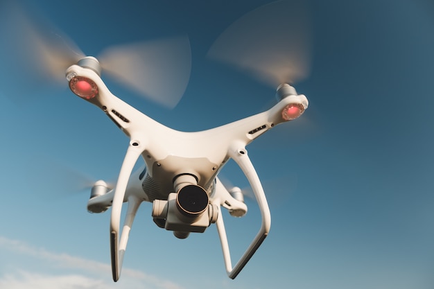 White drone hovering in a bright blue sky Free Photo