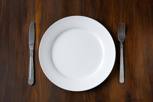 A white plate with a knife and fork on a wooden table | Premium Photo