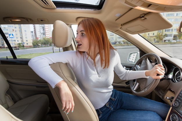 後ろを向いて後方に車を運転する若い赤毛の女性ドライバーの広角ビュー プレミアム写真