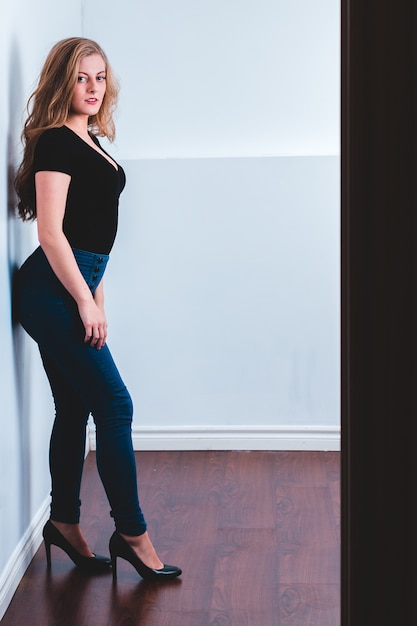 Free Photo Woman In Black Shirt And Blue Denim Jeans Standing Beside White Wall