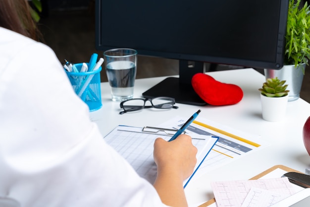 Woman doctor taking notes on clipboard while sitting at her table in office Premium Photo