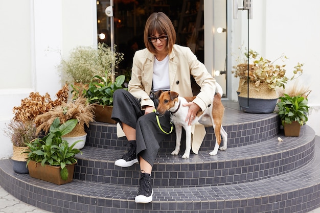 Woman dressed casually sitting on stairs keeps dog's leash Free Photo