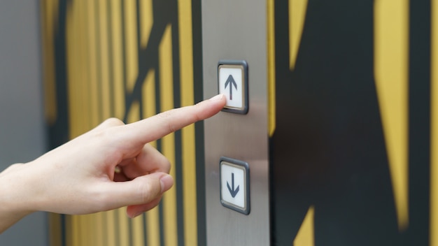 建物の中のエレベーターボタンの上ボタンを押す女性の指 プレミアム写真