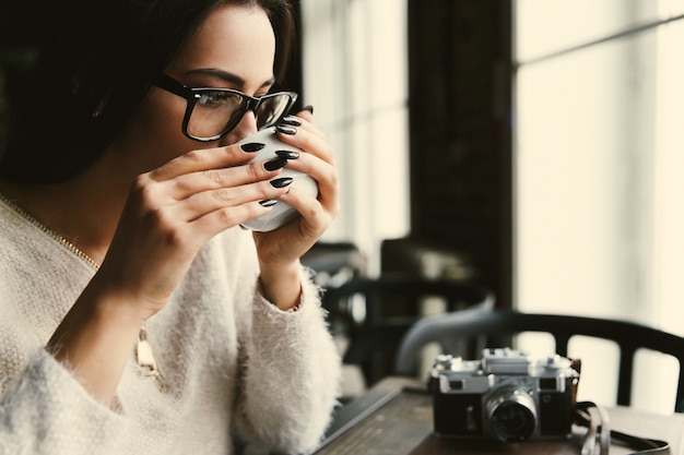 Free Photo | Woman in glasses drinks coffee at the table in bright cafe