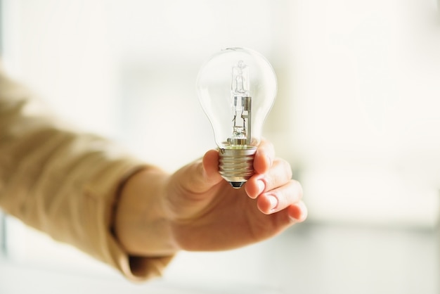 Woman hand holding light bulb on cream background with copy space. creative idea, new business plan, motivation, innovation, inspiration concept. Premium Photo