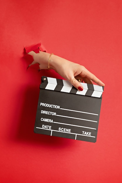 Premium Photo Woman Hand Holding Movie Clapper Through The Hole In Red Paper Wall Movie Production Clapper Board Vlog Film Concept