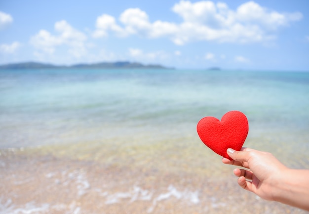 Premium Photo | Woman hand holding a red heart on the beach with ...