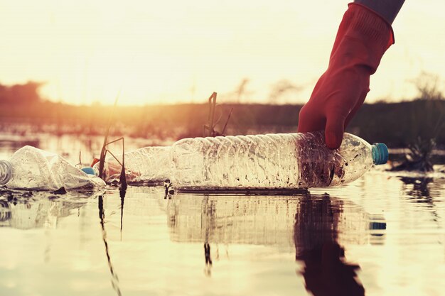 Woman hand picking up garbage plastic for cleaning at river with sunset Premium Photo