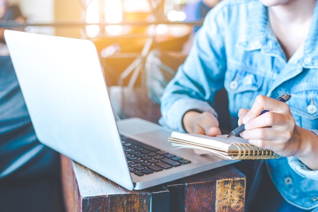 Woman hand works in a laptop computer and is writing on a notepad ...