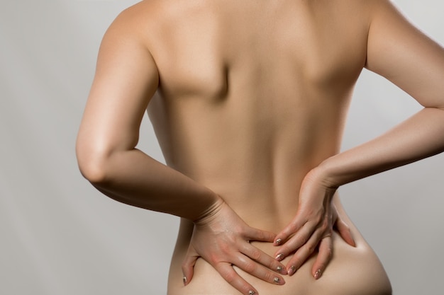 背中の痛み 灰色の背景に分離された痛みを持っている女性 脊柱側弯症 背中の女性の脊髄の問題 彼女の背中に触れている美しい裸の女性 プレミアム写真