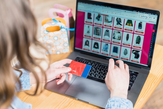 Woman holding credit card in front of laptop with shopping website Free Photo