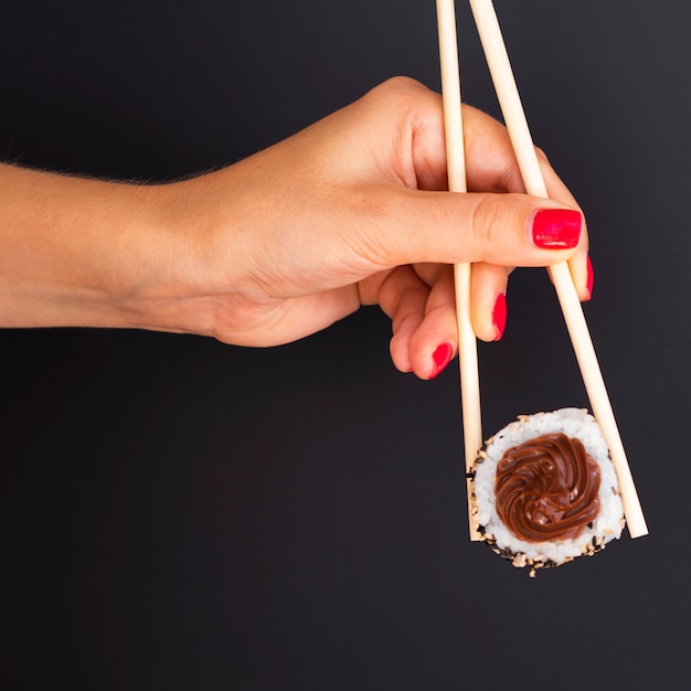 Woman holding a pair of chopsticks with a sushi roll on a black background Photo | Free Download