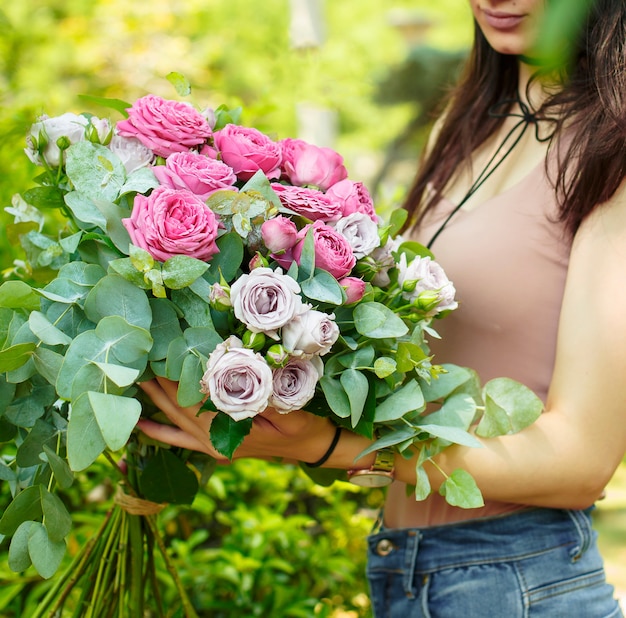 庭にユーカリとピンクのバラの花束を保持している女性を残します 無料の写真