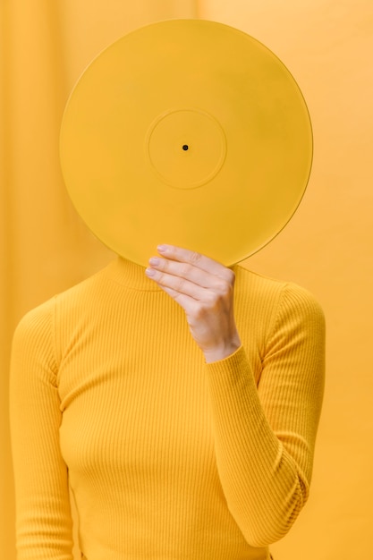 Woman holding vinyl in front of face in a yellow scene Free Photo
