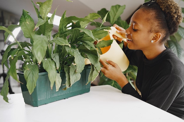 Free Photo | Woman at home. girl in a black sweater. african woman watering  the plant. person with flowerpot.