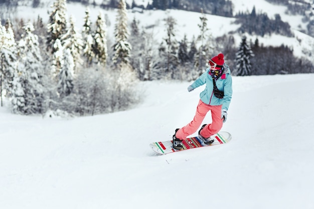 Woman in ski suit looks over her shoulder going down the hill on her snowboard  Free Photo