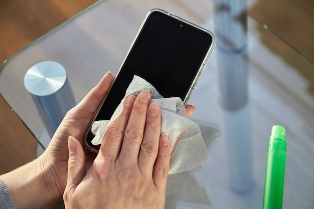 Woman is cleaning a smartphone with a jet of alcohol aerosol hand sanitizer and disposable cloth at home. precautions regarding viruses Premium Photo