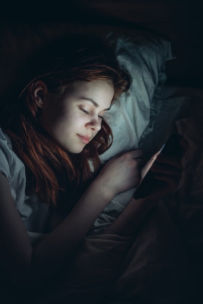 Premium Photo | Woman lies in bed before going to bed with phone in ...