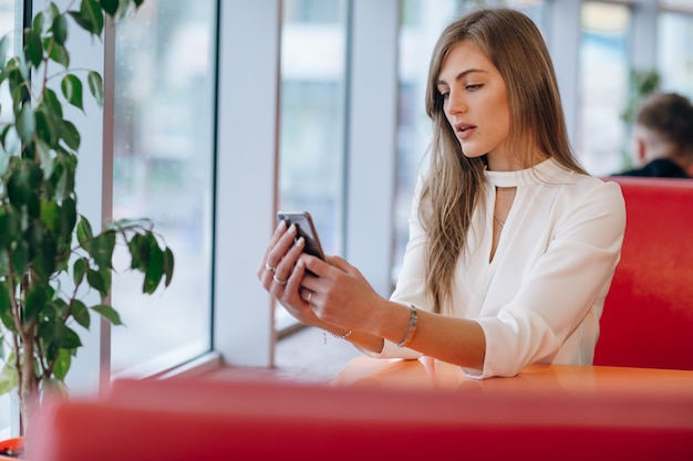 Woman Looking At Her Phone Sitting In A Coffee Shop Photo Free Download