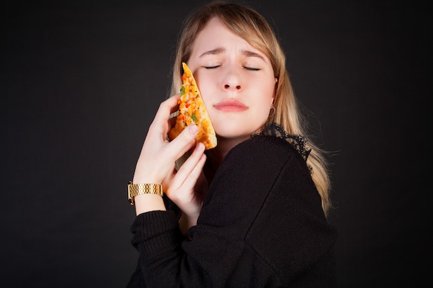 A woman lovingly embraces a slice of pizza, on a black background. Premium Photo