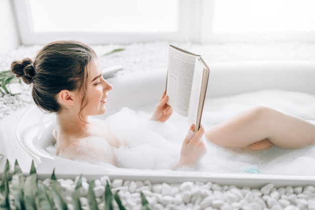 泡でお風呂に横たわって雑誌を読む女性 プレミアム写真