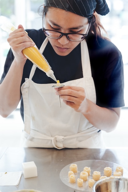 女性パティシエがケーキデコレーションのために黄色いバターの花を作るつもりです プレミアム写真