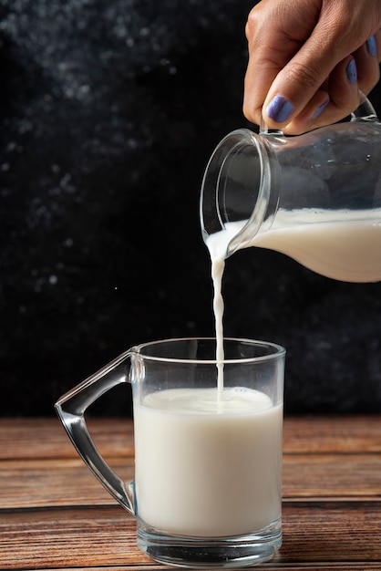 Free Photo Woman Pouring Milk Into The Glass Mug Wooden Table