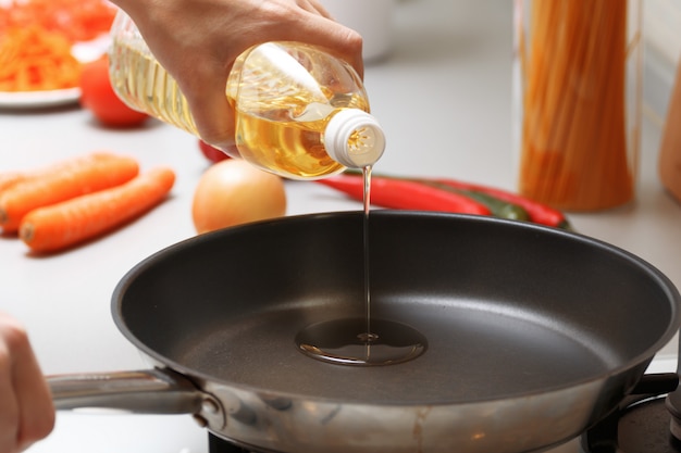 A woman pouring oil from a bottle into the pan in the kitchen, near fresh vegetables and pasta. Premium Photo