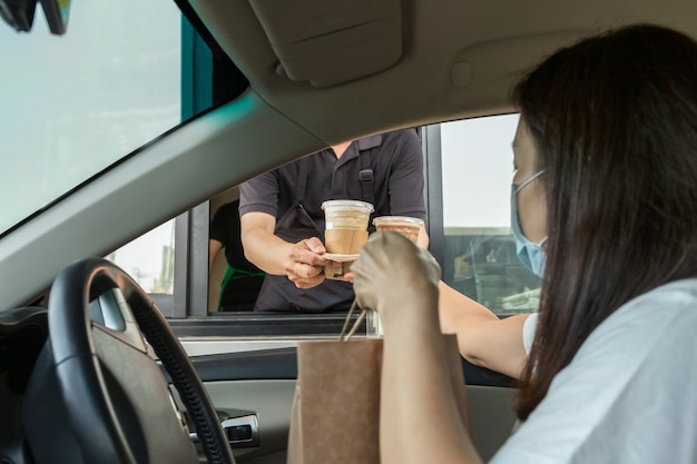 Woman in protective mask taking coffee at drive thru during coronavirus outbreak Premium Photo