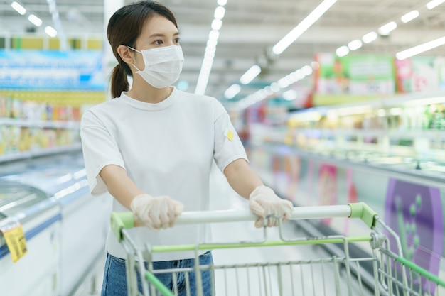 女性は コロナウイルスのパンデミックの後にスーパーで買い物をするショッピングカートで サージカルマスクと手袋の感染から身を守っています プレミアム写真