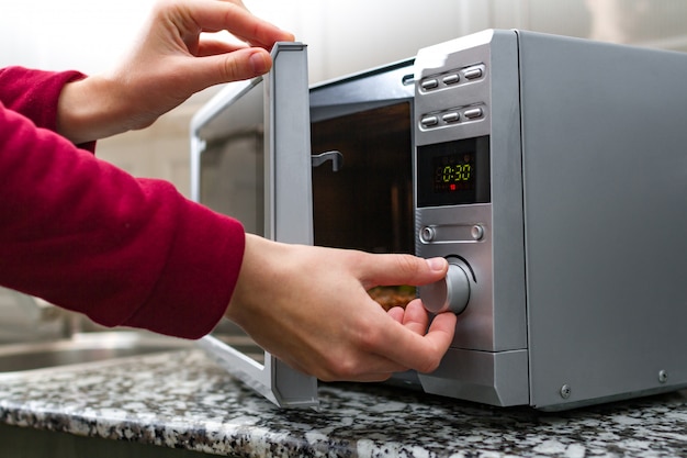 Woman's hand closing the door of the microwave oven and sets the time