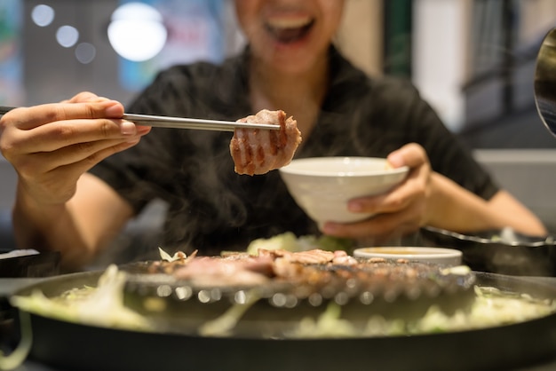 Woman's hand use chopsticks hold korean pork grilled | Premium Photo