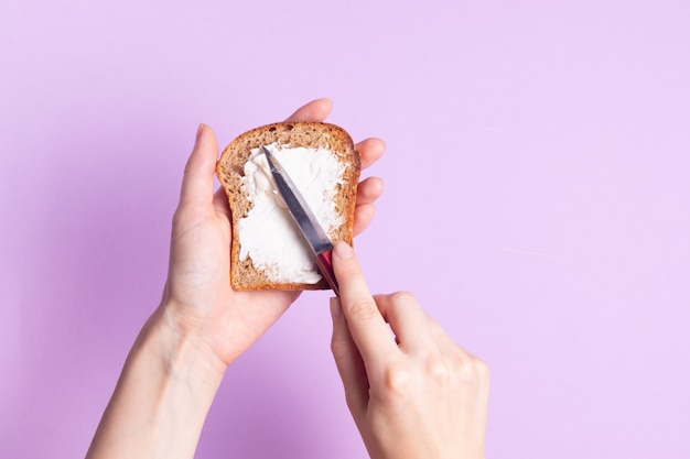 Premium Photo Woman Spreading Cream Cheese On Crispy Toast Bread On Purple Surface
