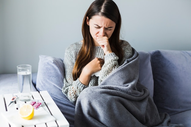 Joven con gripe a lado de una mesa con medicamentos