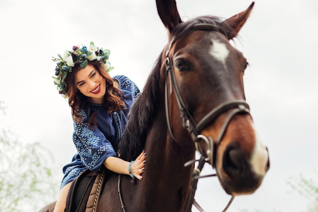 馬に座って笑顔で馬の首をなでる彼女の頭に花輪を持つ女性 プレミアム写真