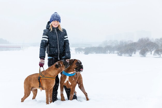 散歩に雪の降る冬の日にボクサー犬を持つ女性 プレミアム写真