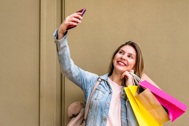 Free Photo Woman With Shopping Bags Taking Selfie At Wall