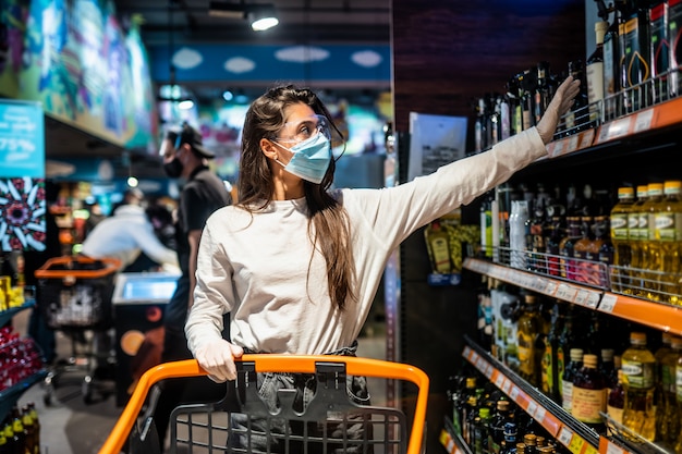 Woman with the surgical mask and the gloves is shopping in the supermarket after coronavirus pandemic. the girl with surgical mask is going to buy the some food. Free Photo