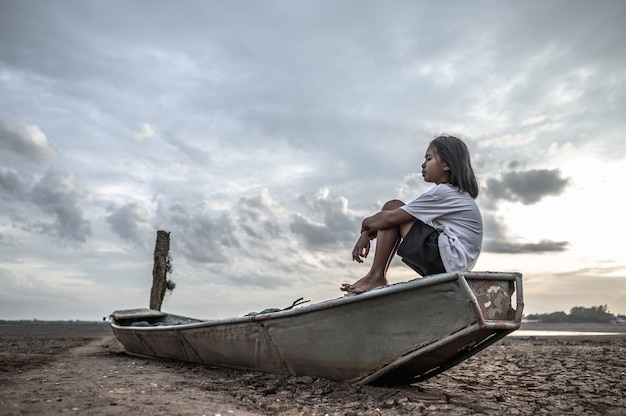 Women sit hugging their knees on a fishing boat and look at the sky on dry land and global warming Free Photo