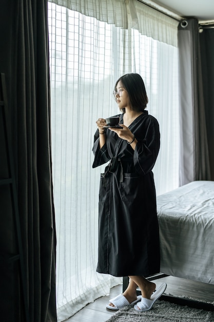 黒いローブを着て 寝室でコーヒーを渡す女性 無料の写真