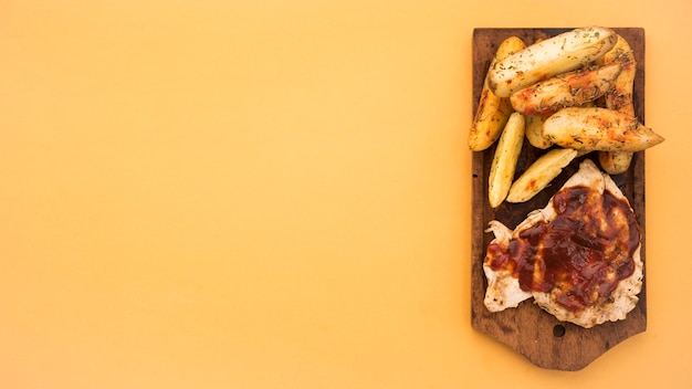 Wooden board with potato wedges and grilled meat Free Photo