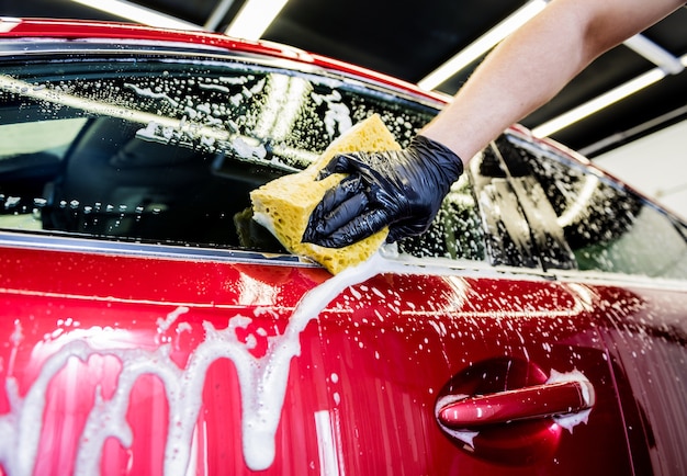 洗車機でスポンジで赤い車を洗う労働者 プレミアム写真