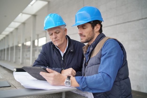 Workmen consulting over blueprint with tablet on modern building sight Premium Photo