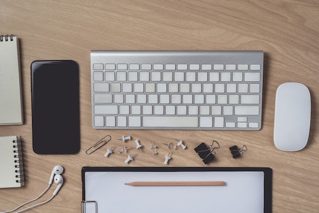 Workspace with diary or notebook and clipboard, mouse computer, keyboard, smart phone, earphone, pencil, pen on wood Premium Photo