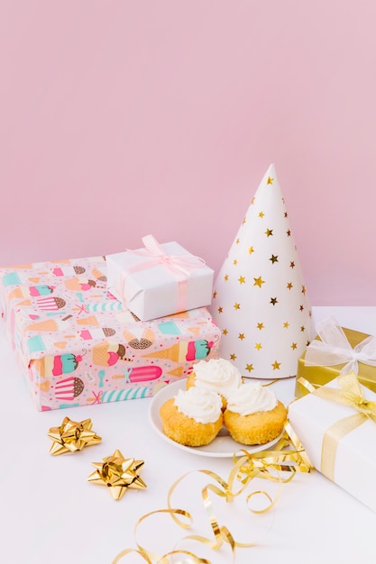 Wrapped Gift Boxes Bow Streamer Party Hat And Cupcakes On Desk