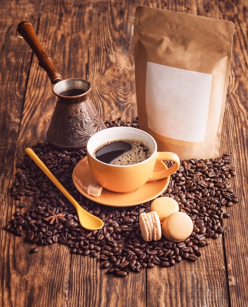 Premium Photo Yellow Cup Of Coffee Macaroons Beans Turkish Coffee Pot And Craft Paper Pouch Bag On Wooden Backgroun