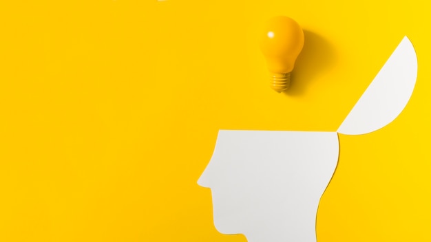 Yellow light bulb over the open paper cut out head against colored background Free Photo